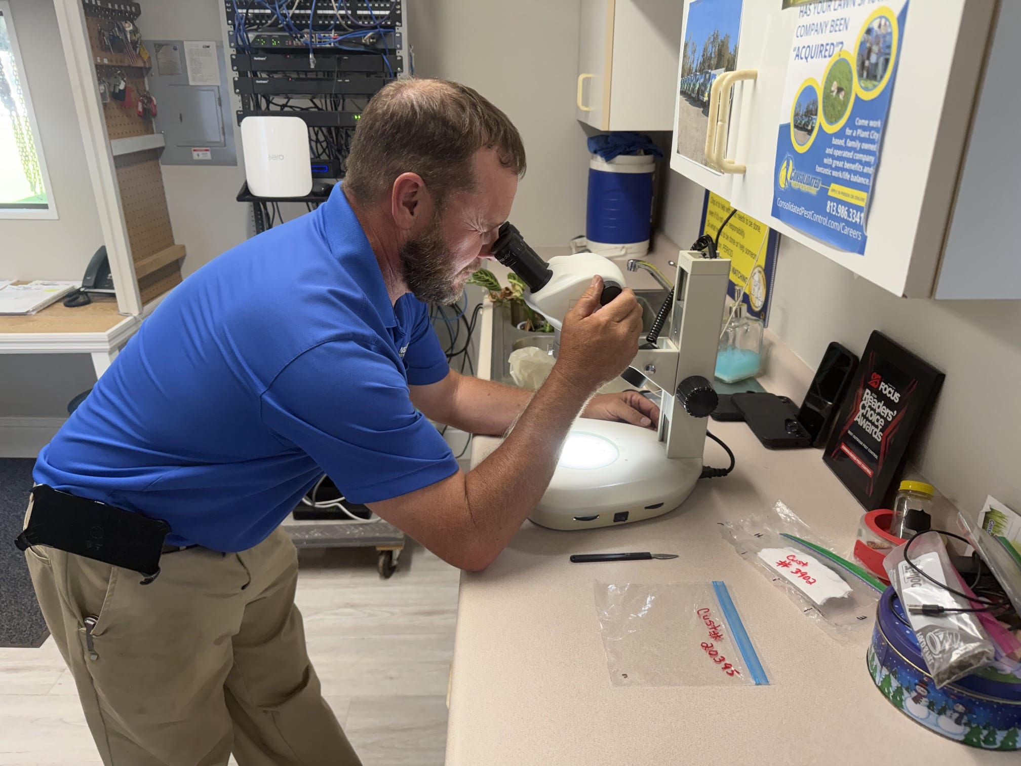 Man in blue shirt examining specimen under microscope at laboratory workbench